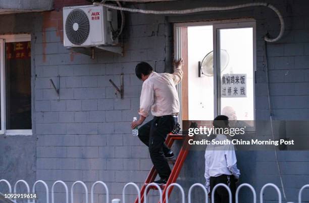 Man steps down the ladder out of a window of a small restaurant to leave after eating dinner in Beijing on May 10, 2017. Beijing is undergoing a...