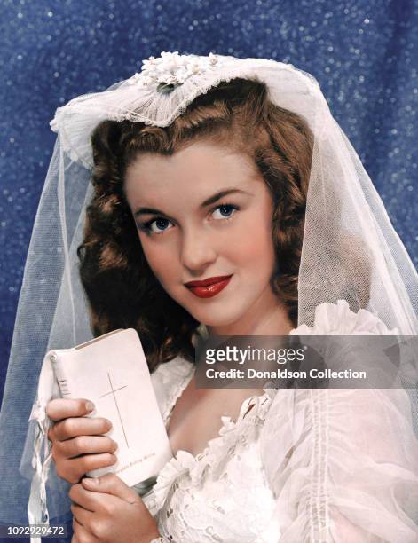 Actress Marilyn Monroe then known as Norma Jeane Mortenson poses for a portrait wearing her first wedding dress and holding a bible in 1946 in print...