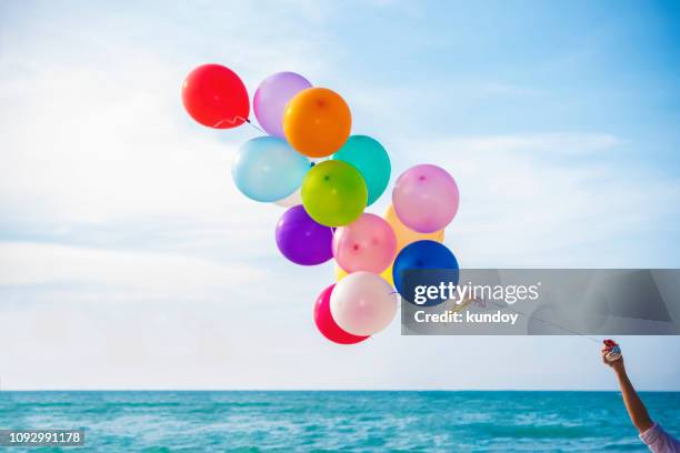 closeup of hand holding colorful balloon on the beach with blue sky background. - balloons in sky stock pictures, royalty-free photos & images