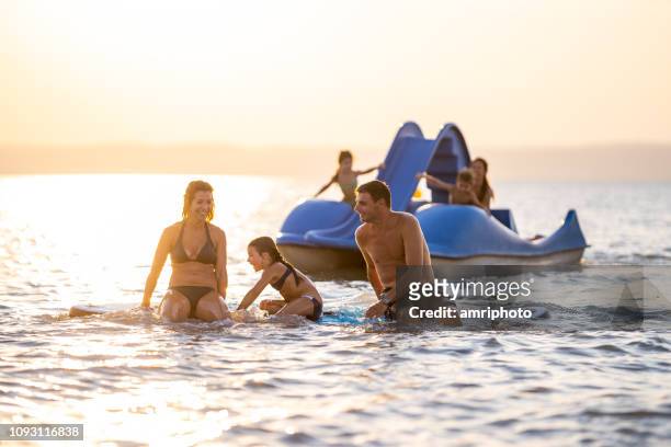 enfants de parents de personnes appréciant le coucher du soleil en bref peu profond lac - pedal boat photos et images de collection
