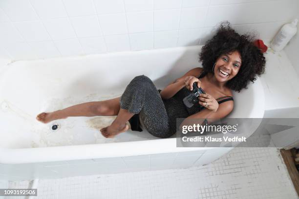 cool young woman laying in bathtub with analog camera - black jumpsuit stockfoto's en -beelden