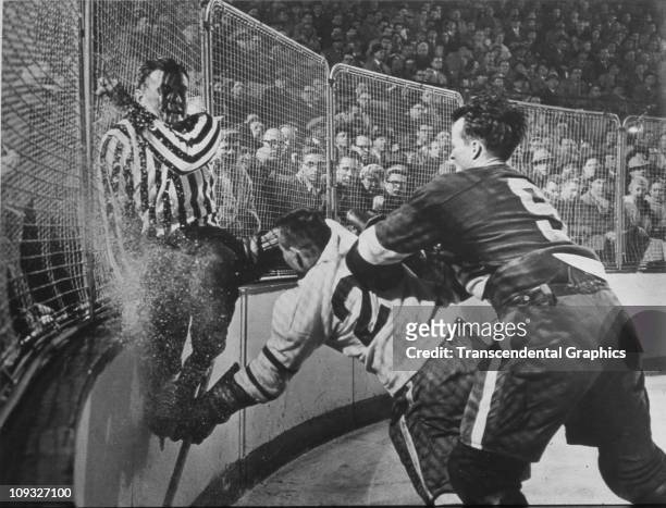 Circa 1955, The Detroit Red Wings' star Gordie Howe, number 9, checks a Chicago Black Hawk opponent into the boards during a National Hockey League...