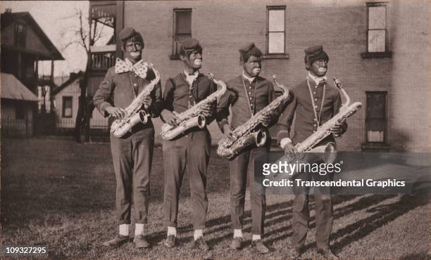 Circa 1910, Four young men in costume and blackface pose with their saxophones in Newark, Ohio as an unnamed minstrel troupe for a photo postcard...