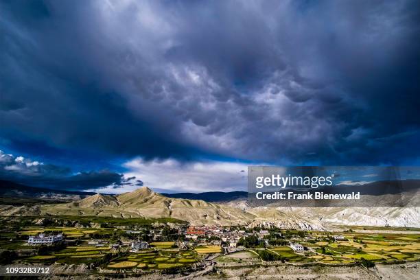 Panoramic aerial view on the town, the agricultural surroundings and the barren landscape of Upper Mustang, dark monsoon clouds approaching.