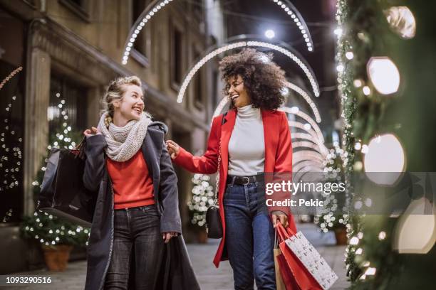 two attractive young women in christmas shopping - red coat stock pictures, royalty-free photos & images