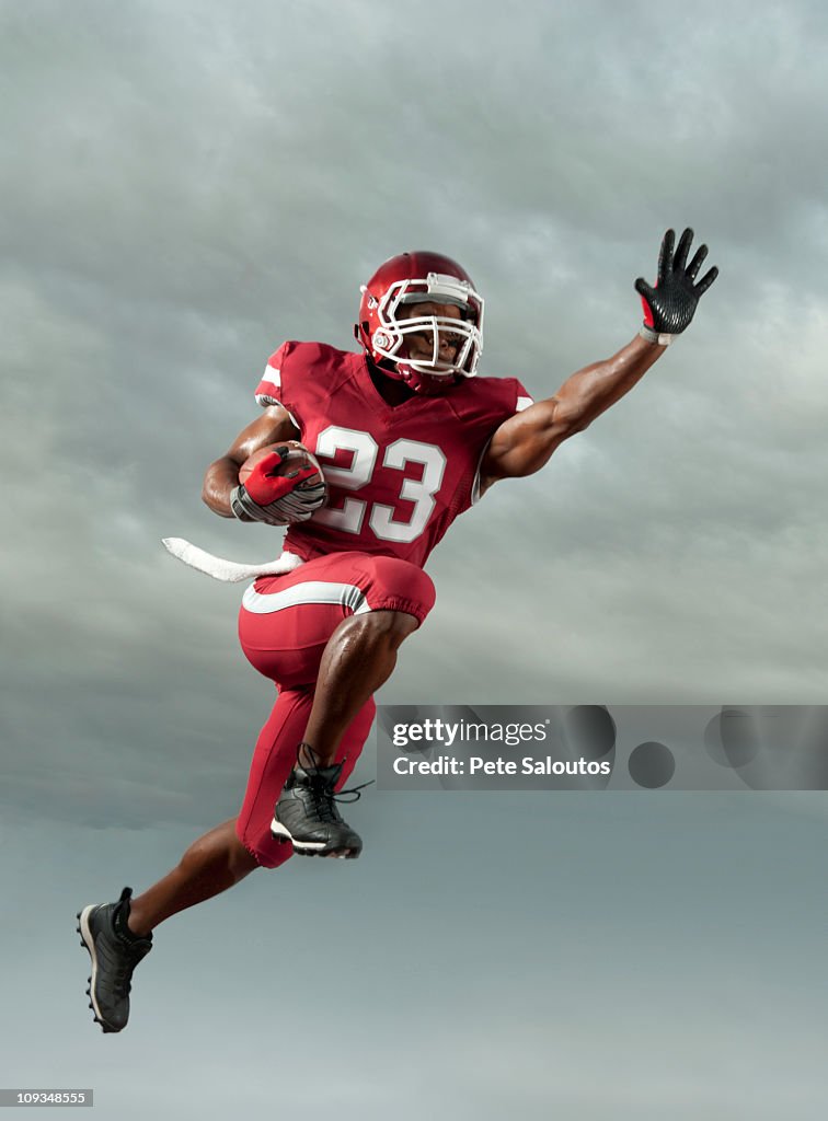 Black football player carrying football in mid-air