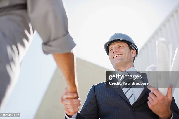 businessman with blueprints shaking hands with worker - architekt helm plan stock pictures, royalty-free photos & images