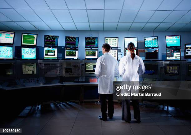 les scientifiques contrôle des ordinateurs dans la salle de contrôle - blouse de laborantin photos et images de collection