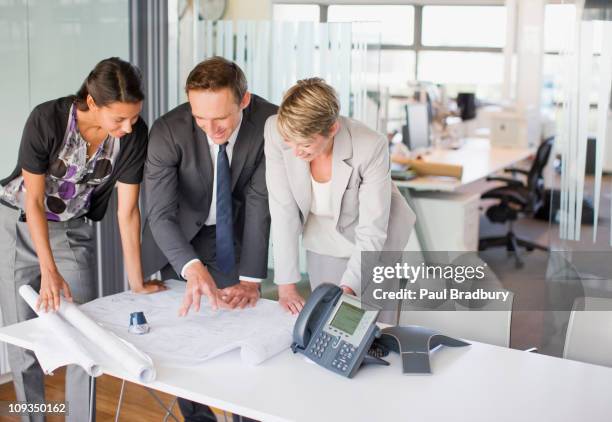 business people reviewing blueprints together in office - conference phone stock pictures, royalty-free photos & images