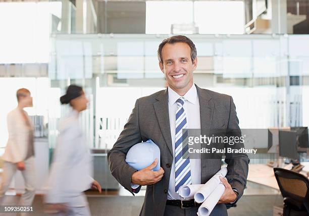 architect holding blueprints in busy office - architekt helm plan stock pictures, royalty-free photos & images