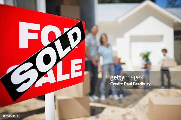 verkauft-schild auf haus mit familie im hintergrund - house with for sale sign stock-fotos und bilder