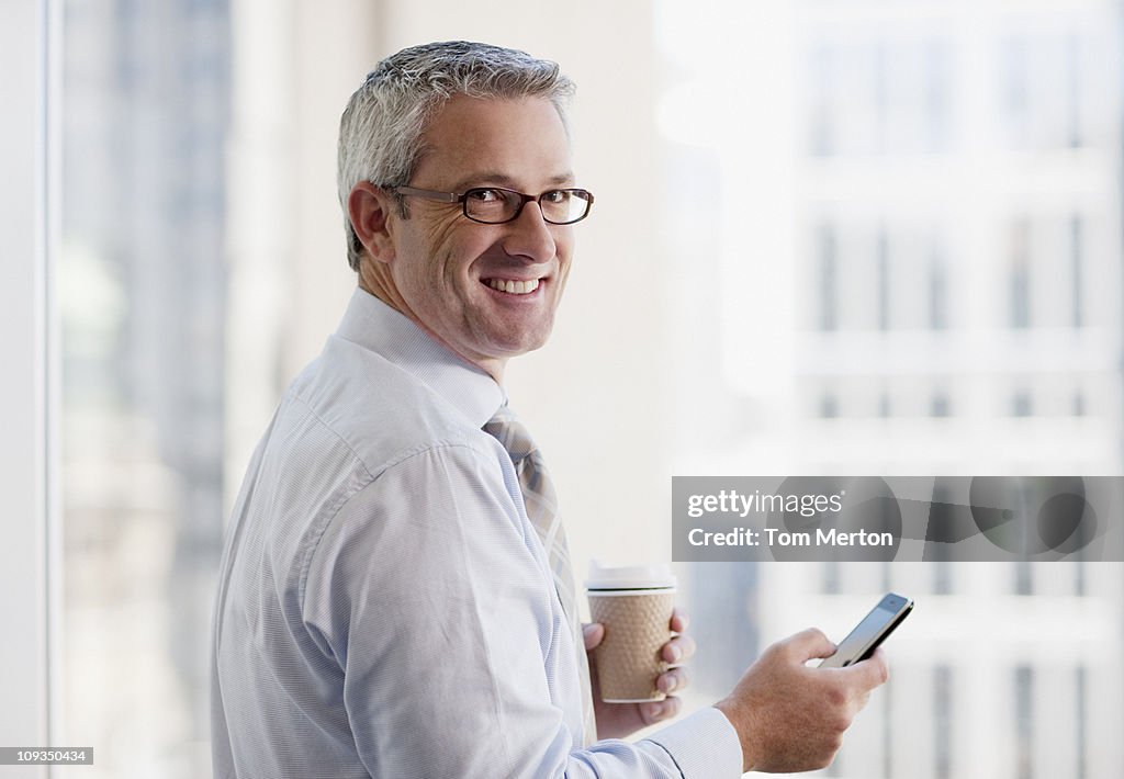 Businessman drinking coffee and text messaging on cell phone