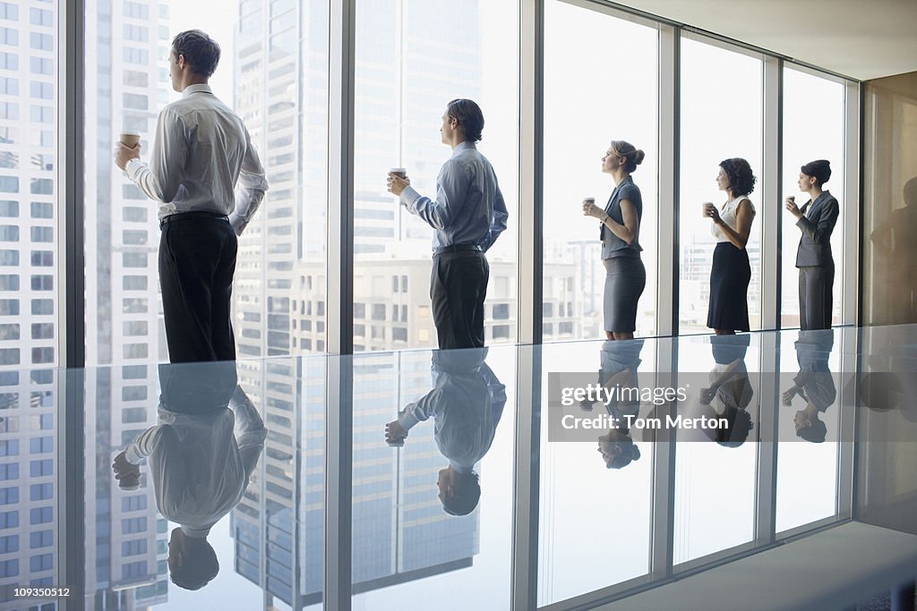 Business people drinking coffee and looking out window in conference room