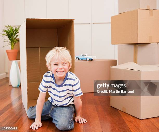 grinning boy playing with boxes in new house - kneeling stock pictures, royalty-free photos & images