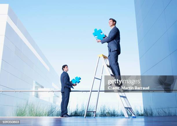 businessmen standing on balcony holding jigsaw puzzle pieces - jigsaw people stock pictures, royalty-free photos & images