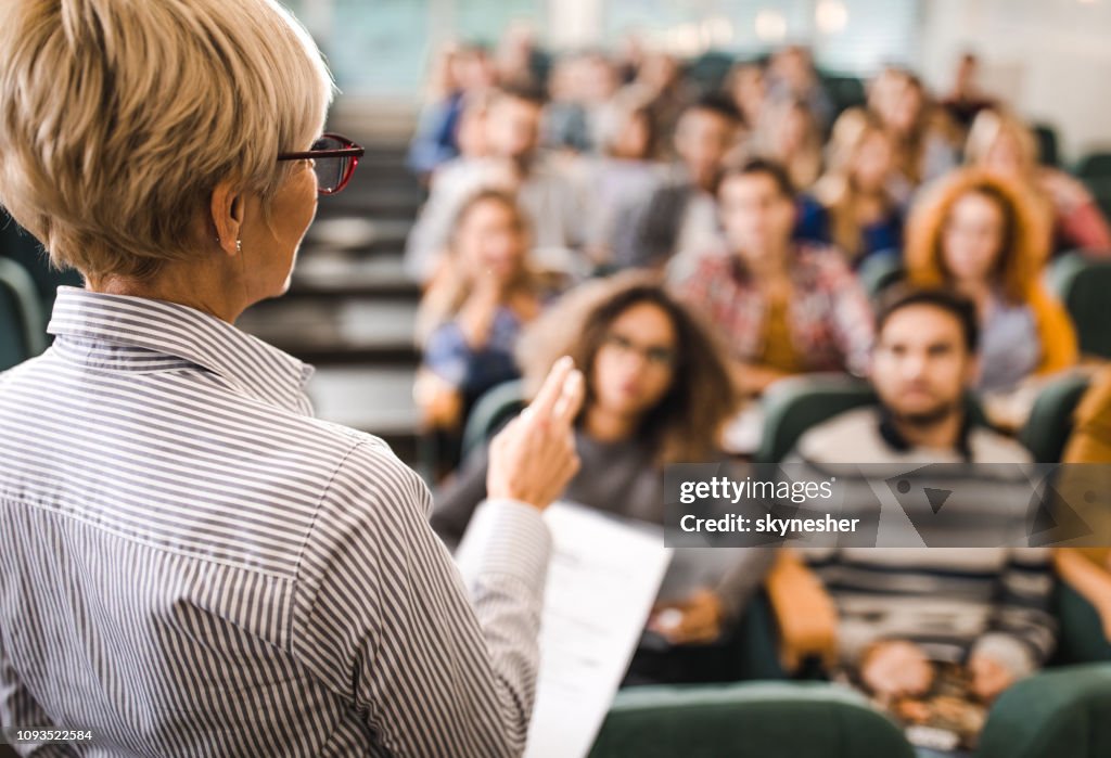 Rear view of mature teacher giving a lecture in a classroom.