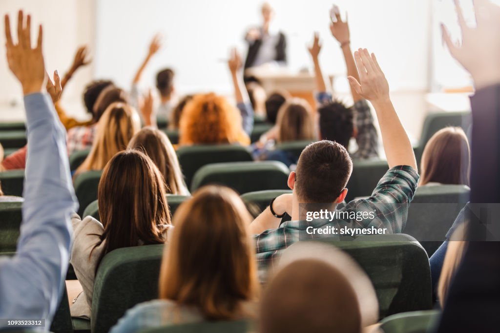 Vista trasera del gran grupo de estudiantes levantando los brazos durante una clase en el anfiteatro.