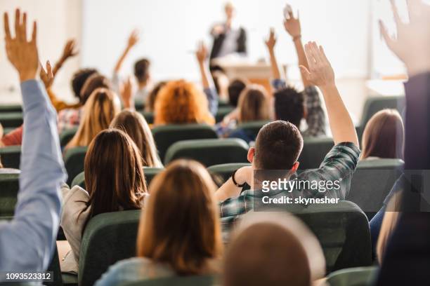 vista posteriore di un grande gruppo di studenti che alzano le braccia durante una lezione all'anfiteatro. - studente universitario foto e immagini stock