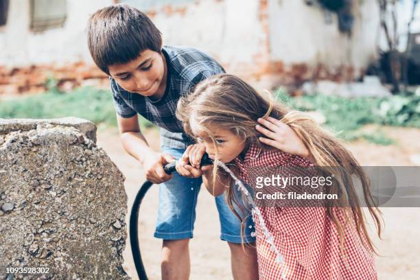 bambini che bevono acqua da un tubo flessibile - casa famiglia foto e immagini stock