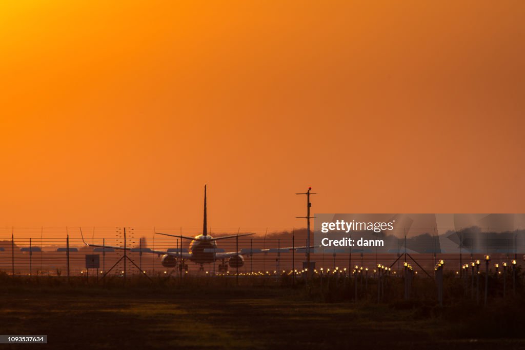 Plane on the track preparing to take off at sunset with red sky in background