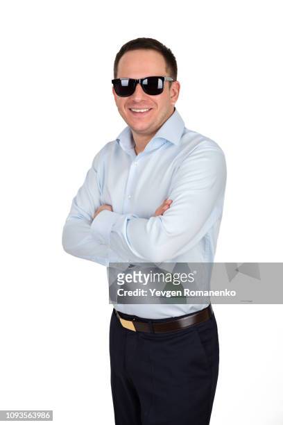 young businessman with cheerful white teeth smile in formal shirt and trousers wears black trendy sunglasses, holds his arms crossed while posing against white background - formal shirt stock pictures, royalty-free photos & images