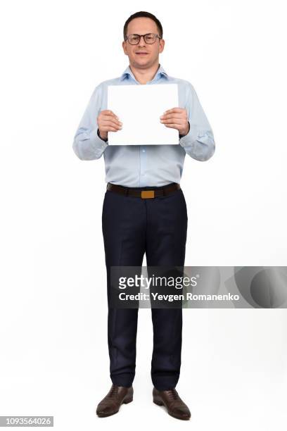 full length portrait of happy smiling young businessman in glasses showing blank signboard, with copy space area for text or slogan, against white background - card board stockfoto's en -beelden