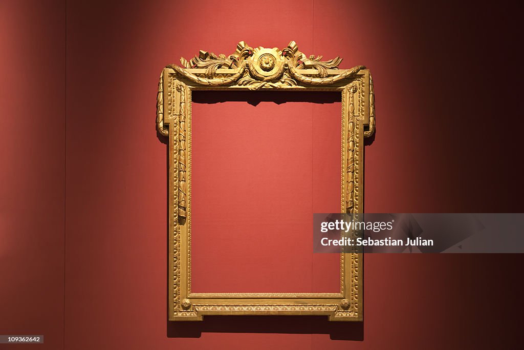 Old golden empty frame against red silk wallpaper