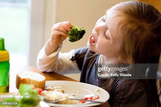 a young girl eating healthy vegetables - broccoli white background stock pictures, royalty-free photos & images