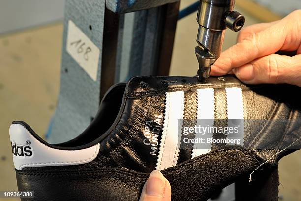 An employee cuts out the shoelace holes for a handmade leather soccer shoe at the Adidas AG factory in Scheinfeld, Germany, on Wednesday, Feb. 23,...