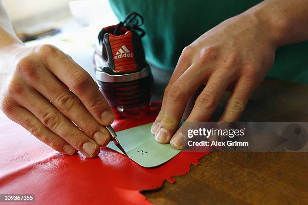 Trainee Patrick Schmerler cuts leather for a handmade football boot at the factory of German sporting-goods maker Adidas AG on February 23, 2011 in...