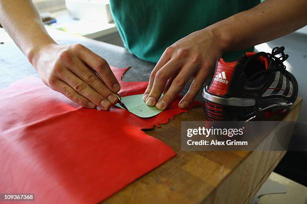 Trainee Patrick Schmerler cuts leather for a handmade football boot at the factory of German sporting-goods maker Adidas AG on February 23, 2011 in...