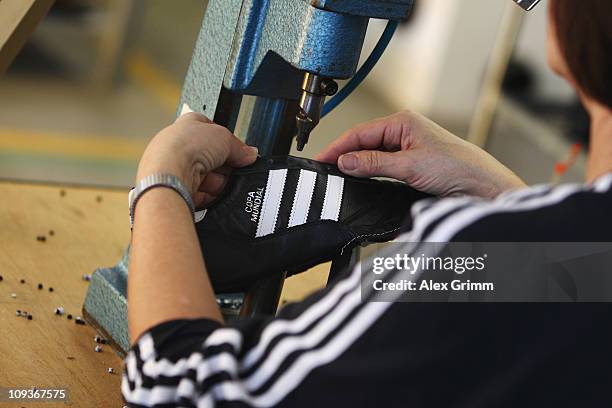 An employee pierces the shoelace holes for a handmade football boot at the factory of German sporting-goods maker Adidas AG on February 23, 2011 in...