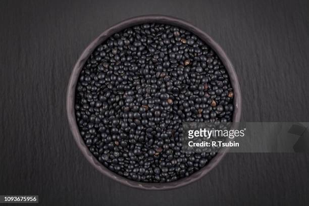 many black beluga lentil seeds in small dark bowl cup isolated on white - lentil stock-fotos und bilder