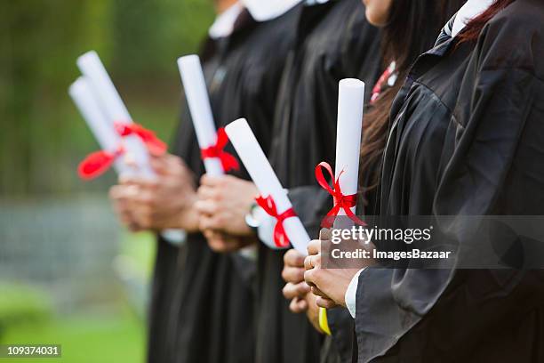 students in graduation gowns holding diplomas - diploma stock pictures, royalty-free photos & images