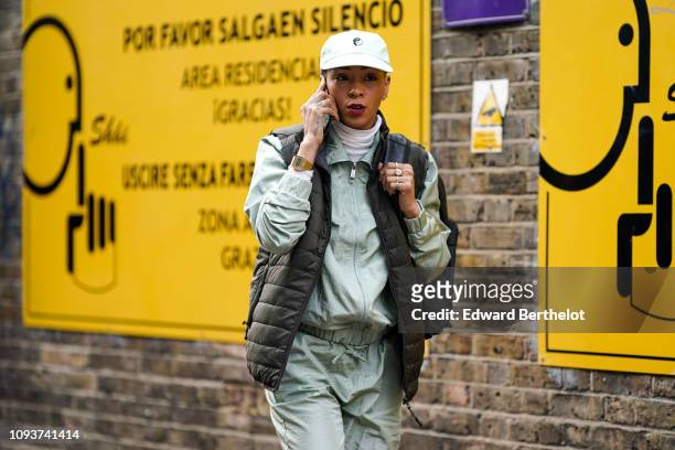 Guest wears a white cap, a sleeveless khaki green puffer jacket, sportswear outfit, during London Fashion Week Men's January 2019 on January 06, 2019...