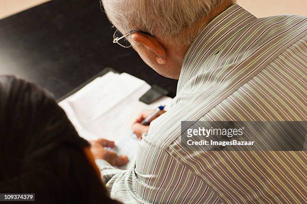 senior couple writing document in living room - man signing paper stock pictures, royalty-free photos & images