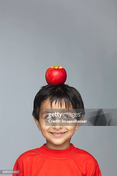 portrait of boy (4-5) with red apple balanced on top of head - child holding apples stock-fotos und bilder