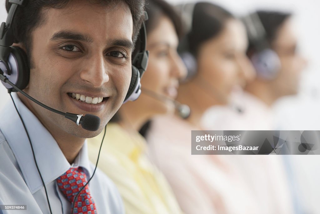 Portrait of male call centre worker wearing headset, colleagues in background