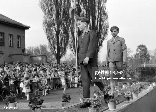 Zwei Jungen zeigen auf einem Laufsteg bei einer Modenschau elegante Kleidung für Kinder, einen Anzug mit langer Hose und eine Kombination von Jacke,...
