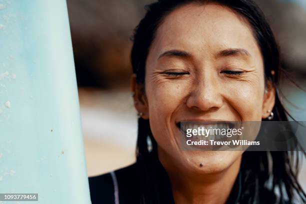 portrait of a mid adult female athlete with her surfboard and showing a positive emotion - female 40 year old beach stock pictures, royalty-free photos & images
