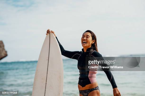 portrait of a mature female athlete with her surfboard with a confident expression - deporte acuático fotografías e imágenes de stock