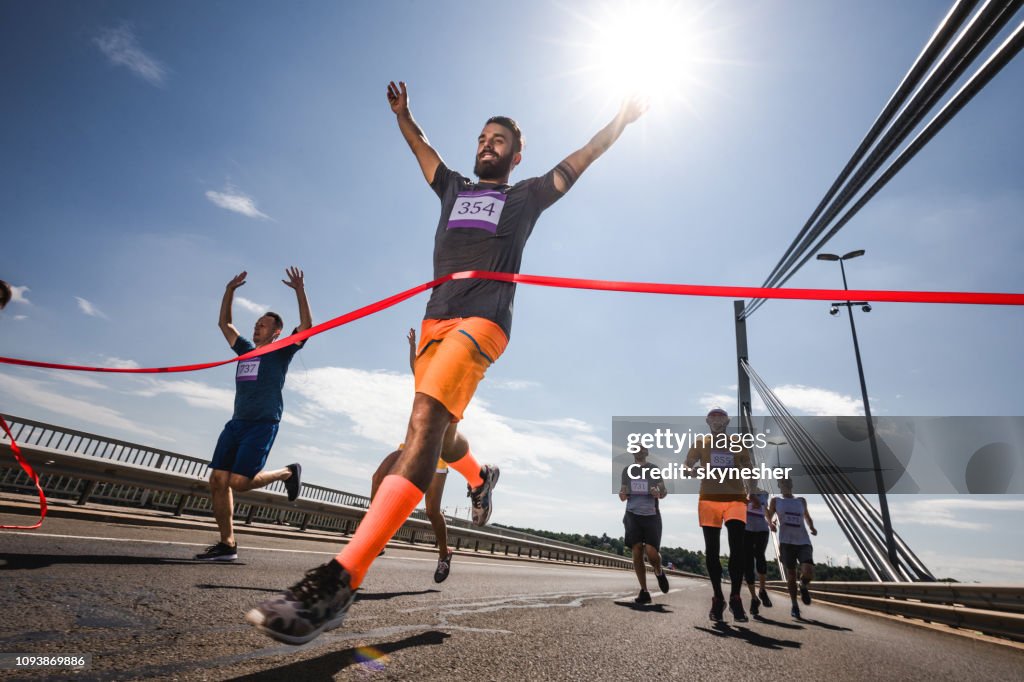 Lage hoekmening van succesvolle man kruising van de afwerkingslijn op marathon race.