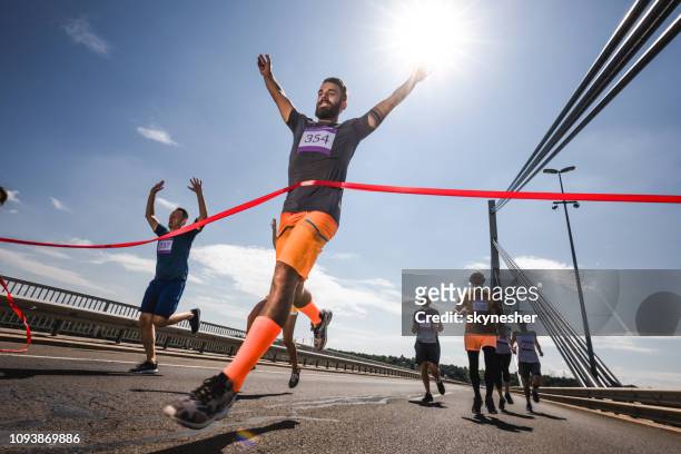 low angle view of successful man crossing the finish line on marathon race. - corrida de rua imagens e fotografias de stock