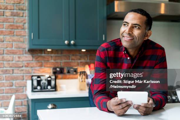 thoughtful man with digital tablet in kitchen - fashion man single casual shirt stock pictures, royalty-free photos & images