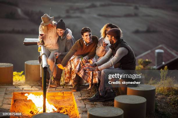 young happy friends talking by the bonfire in autumn. - warming up stock pictures, royalty-free photos & images