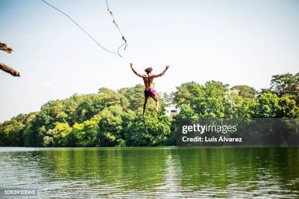 young man jumping into the lake - rope swing fotografías e imágenes de stock