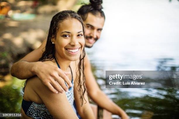 young couple on vacation sitting at the lake - african american women wet stock-fotos und bilder