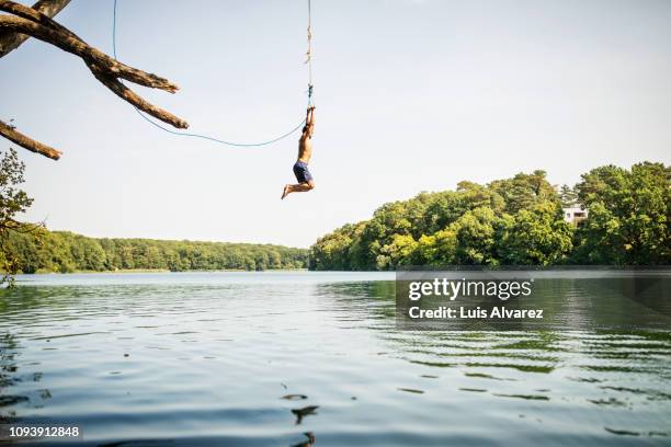 man jumping into the lake from the swinging rope - man adventure fotografías e imágenes de stock