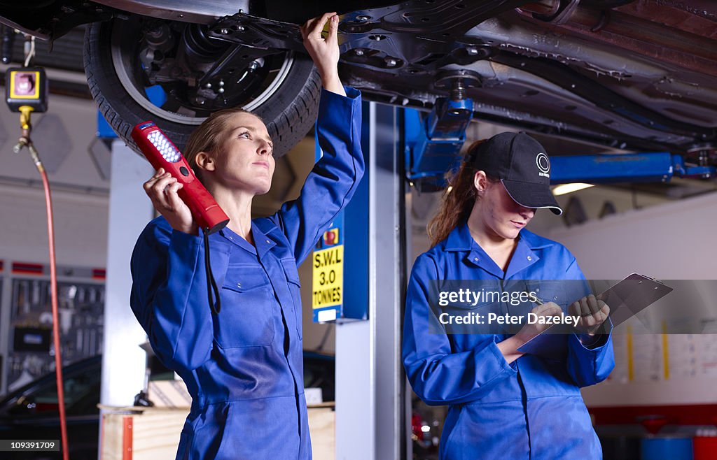 Female mechanics underneath car doing service