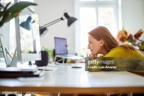 woman looking at desktop monitor at home - solo una donna giovane foto e immagini stock